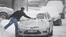 Motorista odklízí sníh z auta na zlínské ulici.