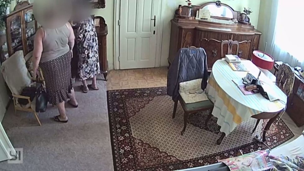 Zlodějka (vlevo) se vrátila do bytu okradené stařenky (94). V obývacím pokoji sleduje, kam žena odloží peněženku.