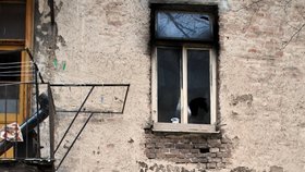 Výmluvný pohled na okno vyhořelého bytu ze dvorku domu: očazené rozbité sklo svědčí o přitápění dřevem a na balkoně vlevo leží roura.