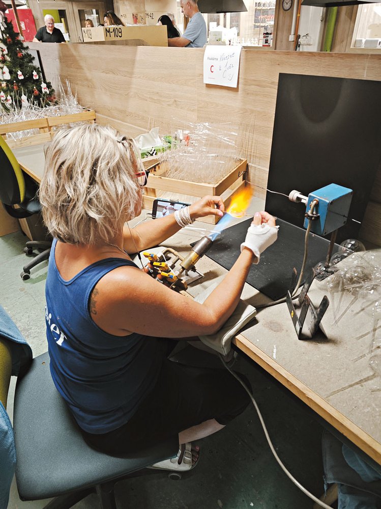 Pracovnice sklárny Koulier nahřívá skleněnou trubičku před foukáním koule
