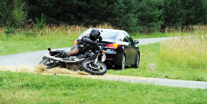 Ze zatáčky vyjíždí na úzké silničce proti motorkáři auto.