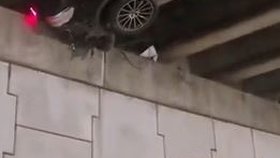 Auto přeletělo přes zábradlí a zůstalo viset nad silnicí. Z vozu trčely nohy řidiče.