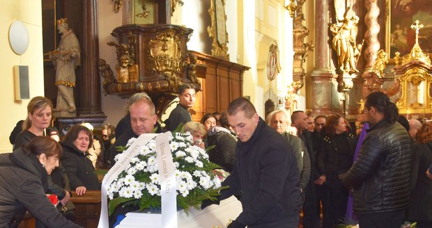 Bílou rakev se zastřelenou ženou odvážejí pracovníci pohřební služby kolem květy z kostela ven.