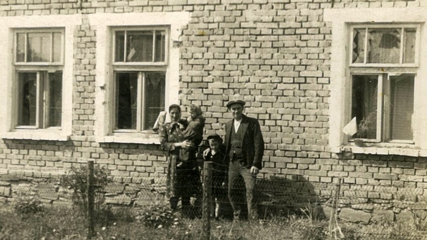 Rodiče pamětníka s jeho sourozenci před jeho rodným domem v Tršicích, na kterém je vidět poškození od granátů