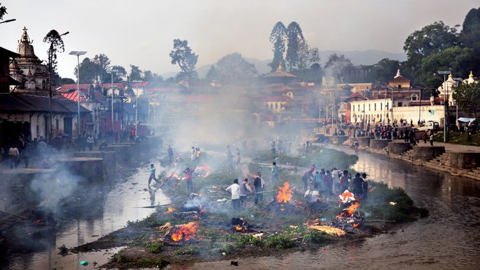 Kremace v Pašupatináthu. Protože většina Nepálců jsou hinduisté, po úmrtí musí následovat tisíciletý rituál – rychlá kremace. Na fotografii je Pašupatináth, nejvýznamnější poutní místo hinduistů v Nepálu, který se rozkládá kolem posvátné řeky Bágmatí nedaleko metropole Káthmándú. Po sobotním zemětřesení zde vyrostlo mnoho hranic, na nichž nebožtíci shořeli. Nejdříve jim musí pohřbívající umýt tělo, pak je zabalí do žluté (oranžové) plachty. Hranici má zapálit nejstarší syn, kolem se shromáždí příbuzní. Když hranice dohoří, jsou zbytky těla hozeny do řeky, v níž se mezitím skoro vždy koupou děti. Symbolem kremace je, že s popelem mrtvých přechází jejich síla a duše na další generace.