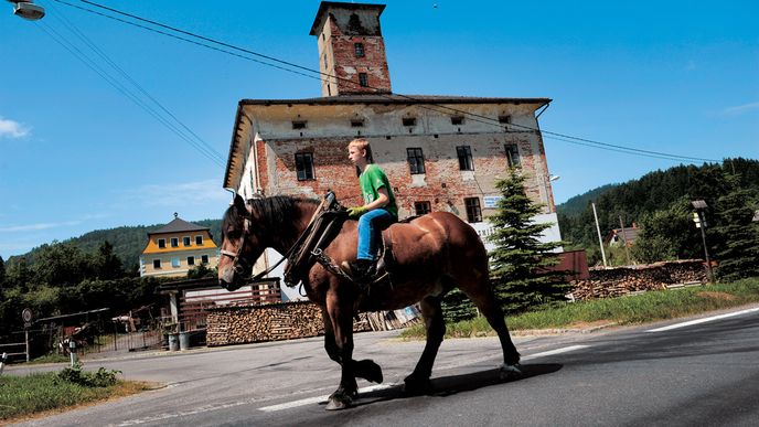 Typický letní den v Sobotíně. Syn místního starousedlíka se projíždí na koni kousek od opraveného venkovského sídla nové vrchnosti – miliardáře Gabriela Večeři.