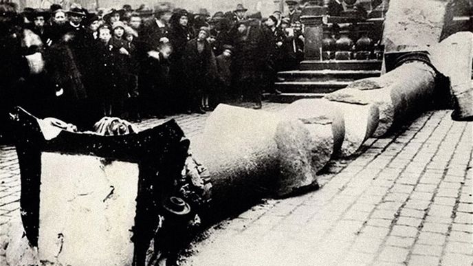 Je 9. listopadu 1918. Staroměstské náměstí zaplnily davy zvědavců.  Úlomek zbořeného sloupu se stal cenným suvenýrem.