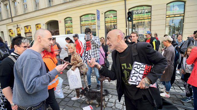 Živé debatě s aktivistou přihlíží v pozadí demonstrantka, která je sice převlečená za kočku, ale vede psa 