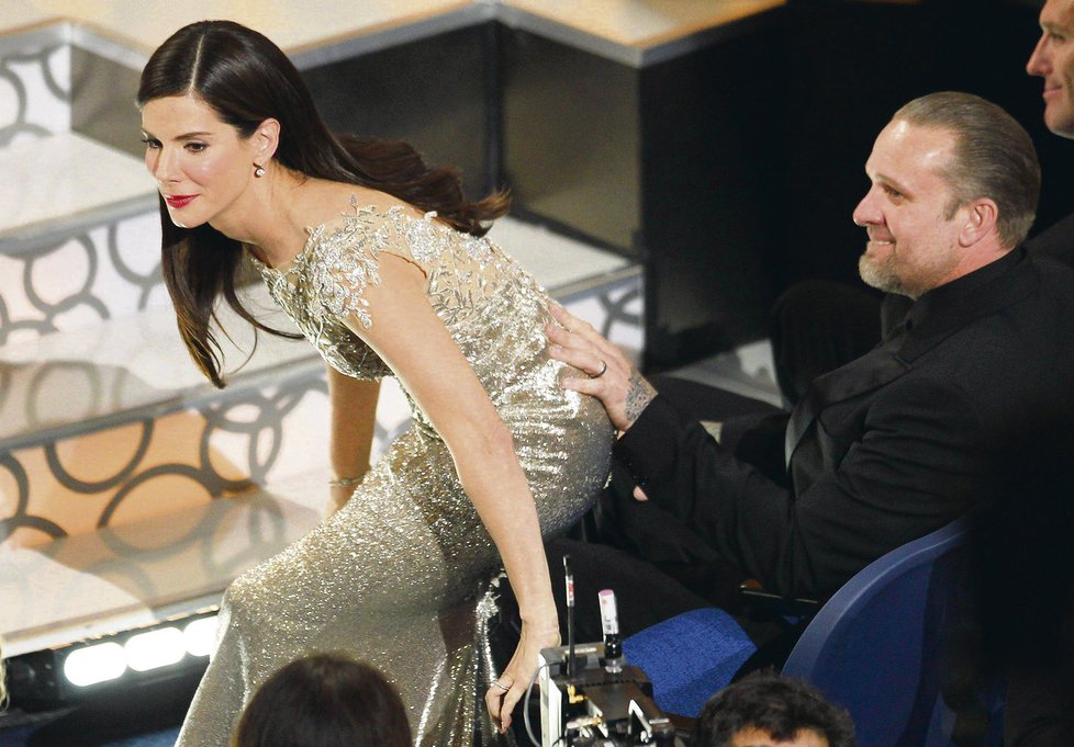 A vítězem se stává... Sandra se zvedá ze své židle a jde si pro svého prvního Oscara. Po zadečku jí hladí manžel Jesse James.