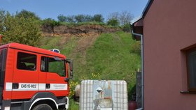 Tyto domy v lokalitě Pískovna ve Strachotíně na Břeclavsku ohrožuje svah nad nimi, který podmáčela voda z vydatných deštů. Nebezpečný svah bude postupně odebírat speciální 60tunový bagr se 17 metrů dlouhým ramenem. Nahoře obhlížejí terén hasič a policista.