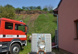Tyto domy v lokalitě Pískovna ve Strachotíně na Břeclavsku ohrožuje svah nad nimi, který podmáčela voda z vydatných deštů. Nebezpečný svah bude postupně odebírat speciální 60tunový bagr se 17 metrů dlouhým ramenem. Nahoře obhlížejí terén hasič a policista.