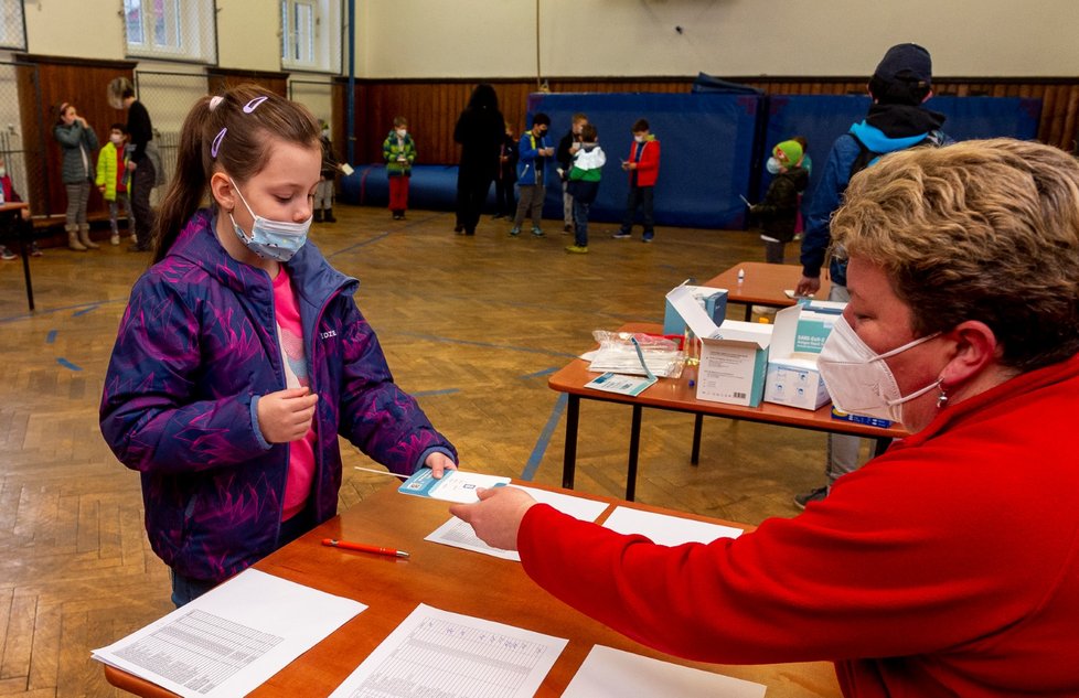 Žákyně Základní školy Chabařovice na Ústecku ukazuje zdravotnici v tělocvičně školy výsledek testu na koronavirus. Vláda rozhodla, že žáci prvního stupně základních škol se od tohoto dne vrátí do lavic v rotační formě, ve školách je jen polovina žáků (12. 4. 2021).