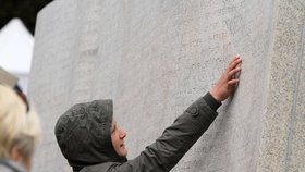 Žena se dotýká památníku, jsou tam vypsána jména obětí