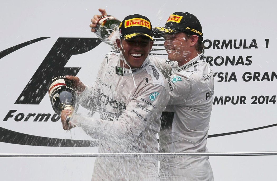 Na pódiu se svorně stříkají šampaňským, brzy ale může dojít k fatálnímu střetu. Lewis Hamilton a Nico Rosberg (vpravo) po GP Malajsie