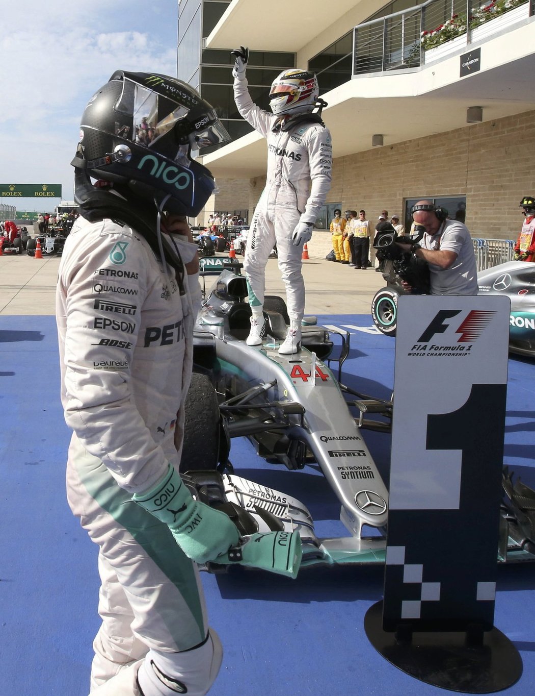 Lewis Hamilton (vzadu) slaví svůj americký triumf, zatímco kolem něj prochází stříbrný stájový kolega Nico Rosberg