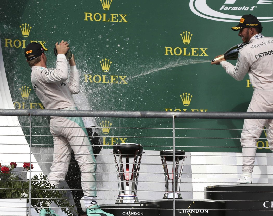 Lewis Hamilton a Nico Rosberg sprchují šampaňským jednoho z členů týmu na stupních vítězů po GP USA