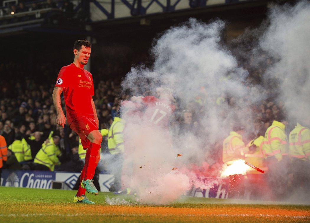 Obránce Liverpoolu Dejan Lovren odklízí světlice z trávníku