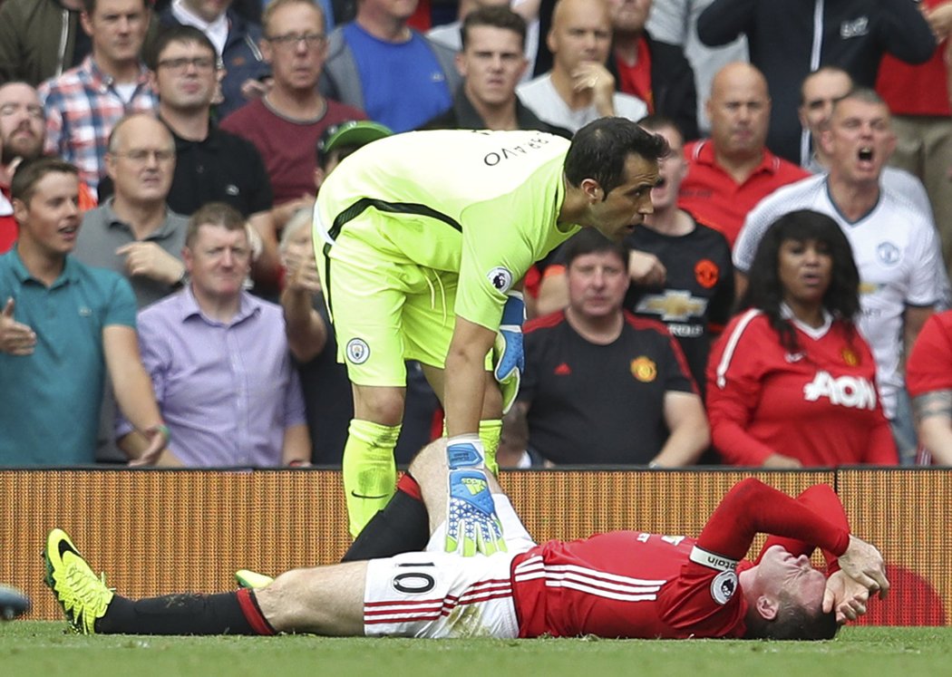 Gólman Manchesteru City se sklání nad kapitánem United Waynem Rooneyem během manchesterského derby v Premier League.