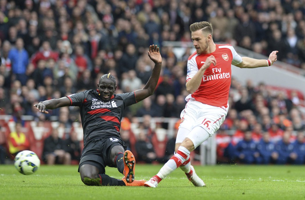 Fotbalistu Arsenalu Aaron Ramsey zakončuje akci v utkání Premier League. Zabránit se mu snažil Mamadou Sakho z FC Liverpool.