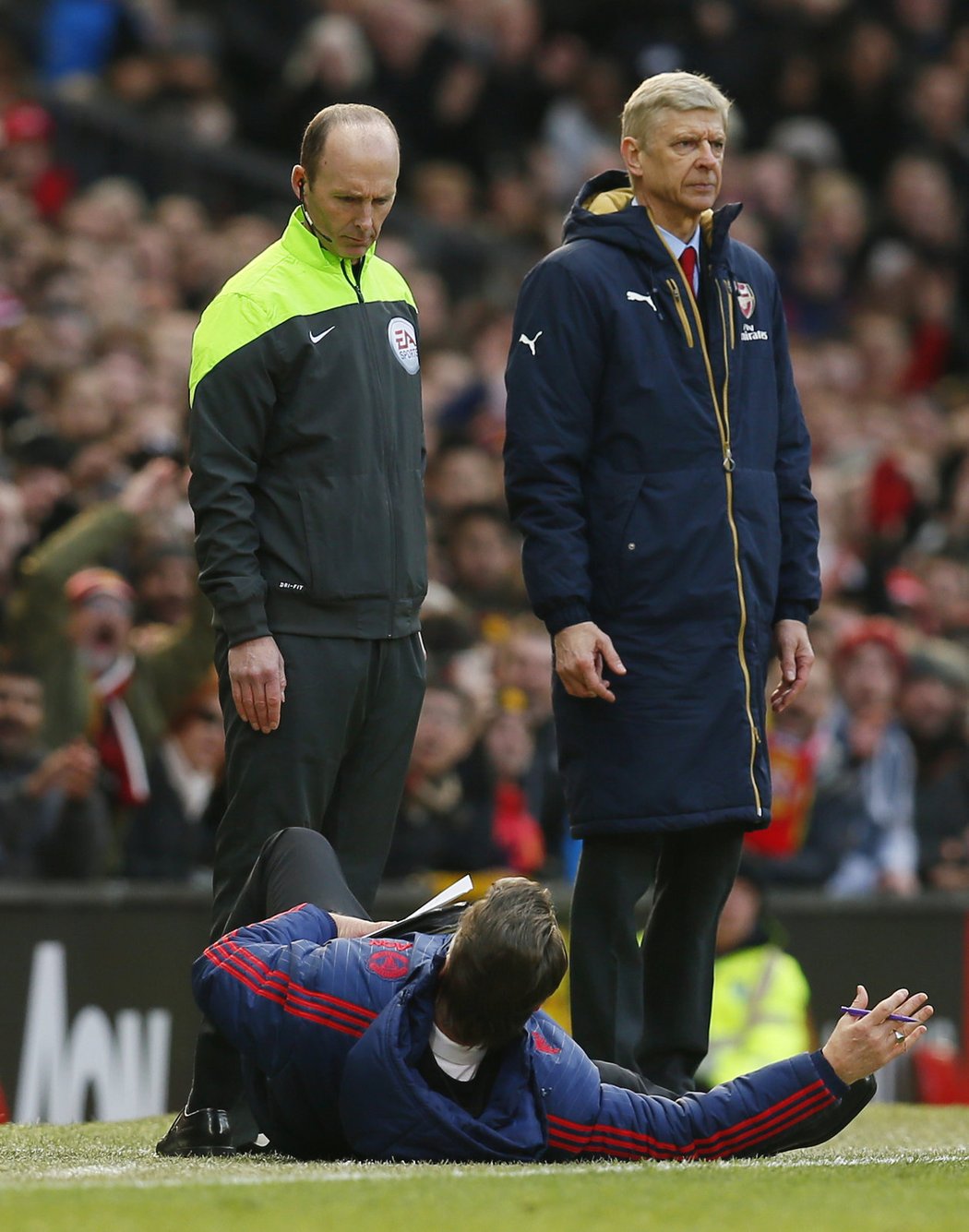 Čtvrtý sudí Mike Dean a trenér Wenger přihlíží, jak Van Gaal spadl na zem