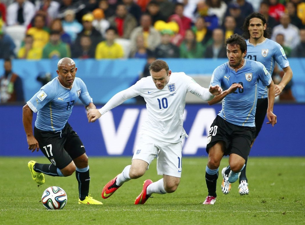 Wayne Rooney se snaží prokličkovat mezi několika uruguayskými fotbalisty