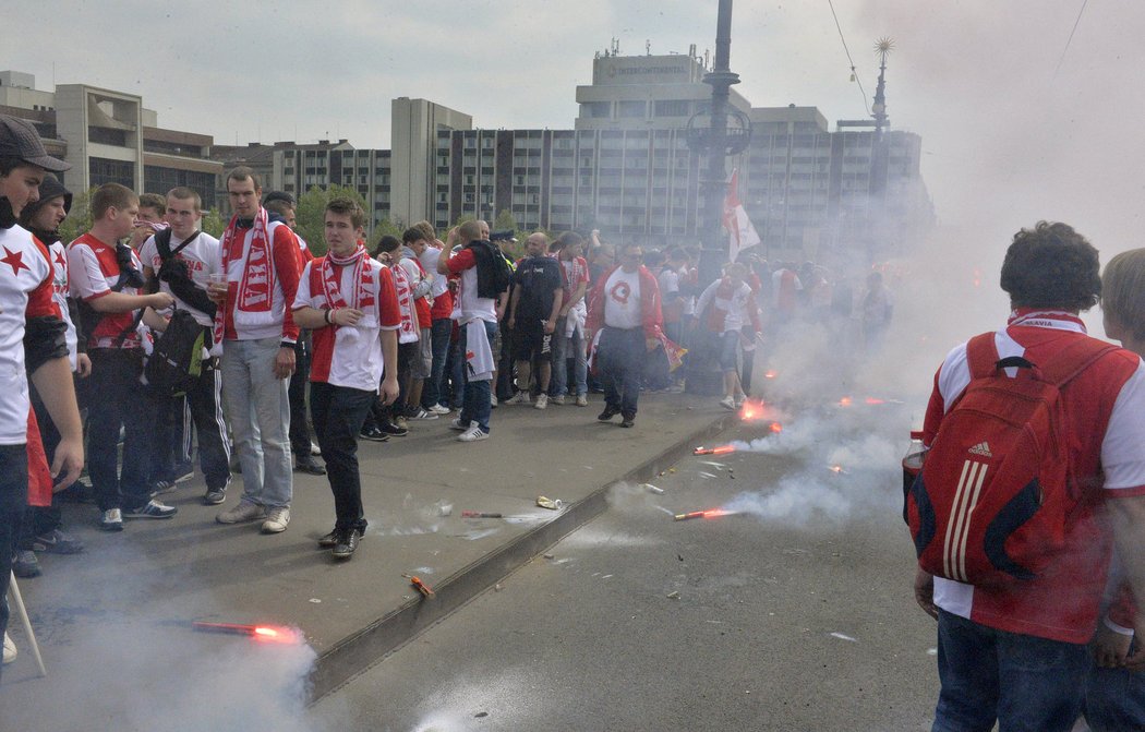 Fanoušci Slavie obcházejí hořící světlice, které na Čechově mostě v Praze vyprovokovaly policii k zásahu