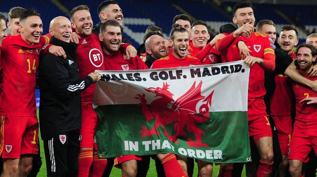 Gareth Bale oslavuje se spoluhráči z velšské reprezentace postup na EURO s vlajkou, která má znázorňovat jeho priority v pořadí Wales, golf, Madrid