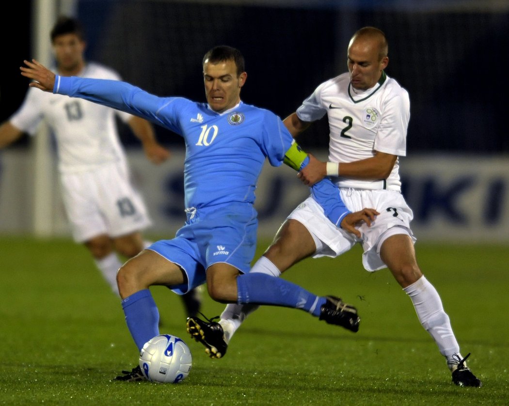 Kapitán San Marina Andy Selva (v modrém) se snaží odkopnout míč i přes obranu Slovince Miša Brečka.