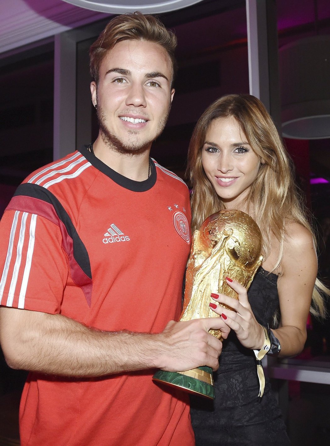 Střelec zlatého gólu Mario Götze pózuje na mistrovském večírku s trofejí a přítelkyní Ann-Kathrin Brömmelovou