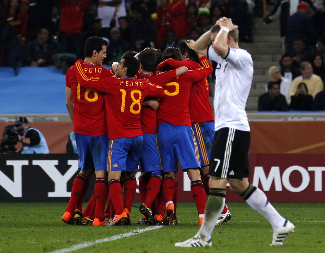 Bastian Schweinsteiger se drží za hlavu zatímco kráčí kolem hloučku radujících se Španělů po gólu Puyola