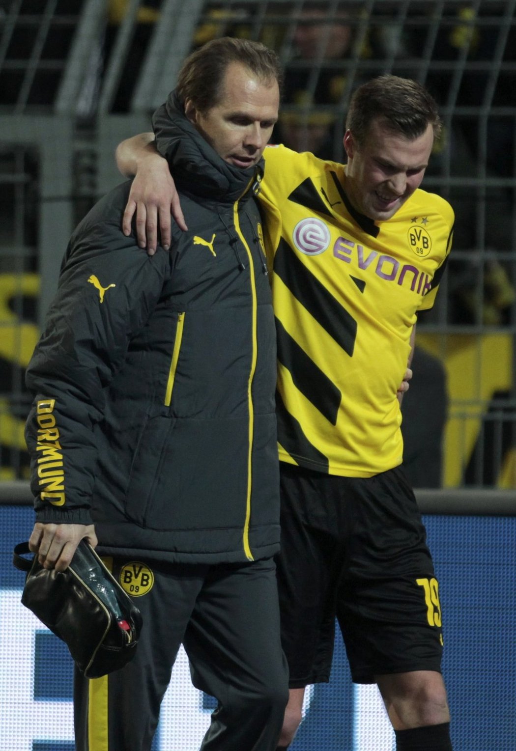 Zraněný Kevin Grosskreutz opouští trávník v doprovodu klubového doktora v zápase Dortmundu s Augsburgem