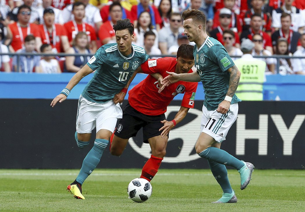 Němci Marko Reus a Mesut Ozil v souboji s Jung Woo-youngem