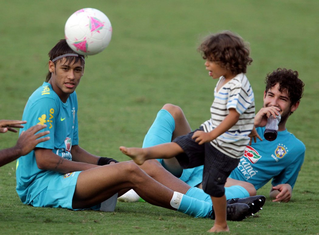 Brazilci Neymar (vlevo) a Alexandre Pato pozorují hrajícího si Enza - syna jejich spoluhráče Marcela