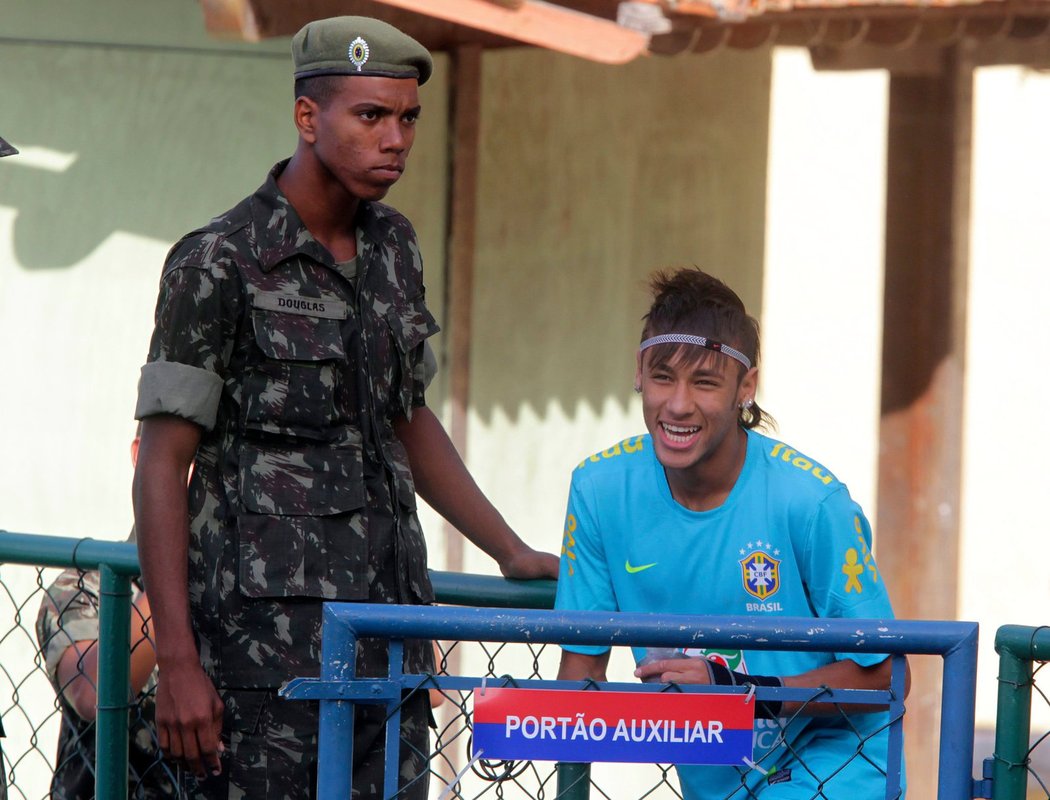 Neymar se smíchem přichází na trénink brazilské reprezentace před blížícím se olympijským turnajem. Brazilci trénovali na vojenské základně v Rio de Janeiru, hlídkující voják takovou radost ze života jako hvězdný talent evidentně nemá...