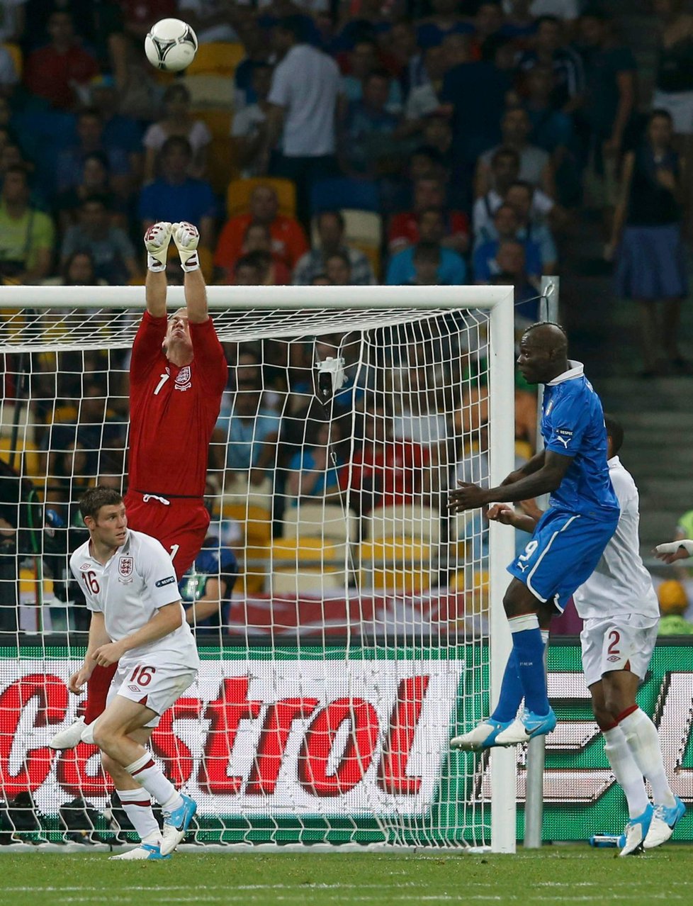 Anglický brankář Joe Hart zasahuje proti míči z italských kopaček, vpravo skáče Mario Balotelli