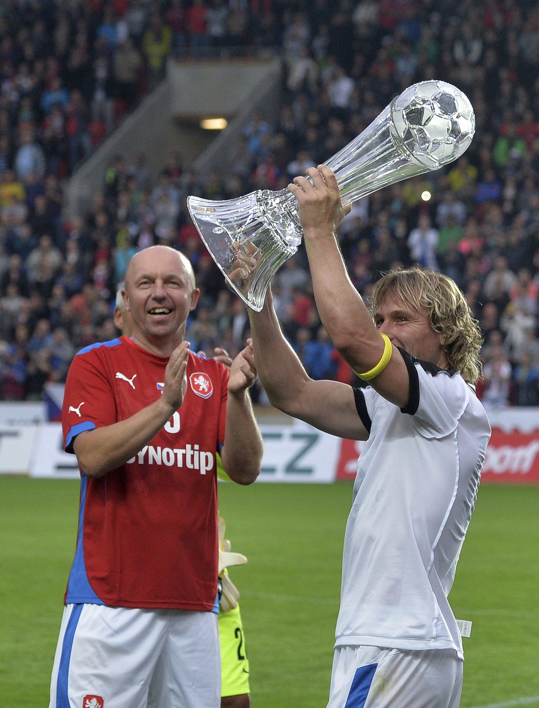 Kapitán Pavel Nedvěd zvedá nad hlavu pohár pro vítěze exhibice Setkání legend, tleská mu Miroslav Kadlec