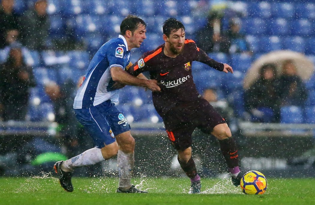 Lionel Messi se na promáčeném trávníku snaží uniknout Victoru Sanchezovi