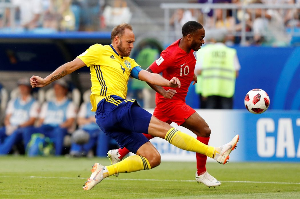 Švédský kapitán Andreas Granqvist odkopává míč před anglickým rychlíkem Raheemem Sterlingem