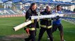 Zlámalem zlomená tyč odnášená ze stadionu za pomoci hasičů