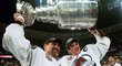 Ray Bourque (vlevoú s Joem Sakicem zvedají nad hlavu Stanley Cup z finále 2001. Muž s céčkem na dresu při převzetí trofeje udělal úžasné gesto, když Pohár okamžitě předal do rukou legendárního obránce