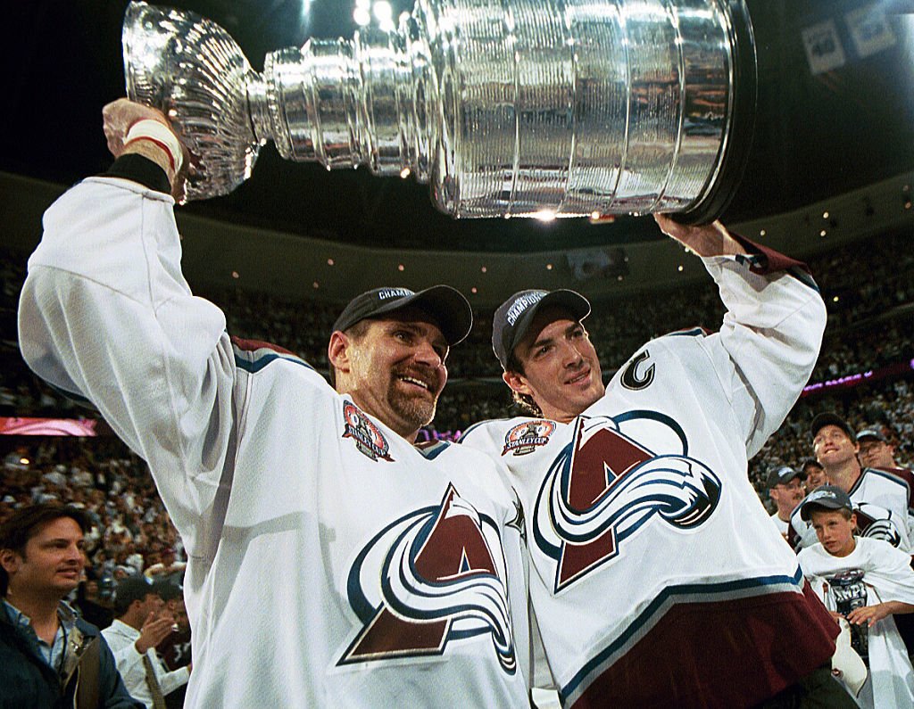 Ray Bourque (vlevoú s Joem Sakicem zvedají nad hlavu Stanley Cup z finále 2001. Muž s céčkem na dresu při převzetí trofeje udělal úžasné gesto, když Pohár okamžitě předal do rukou legendárního obránce