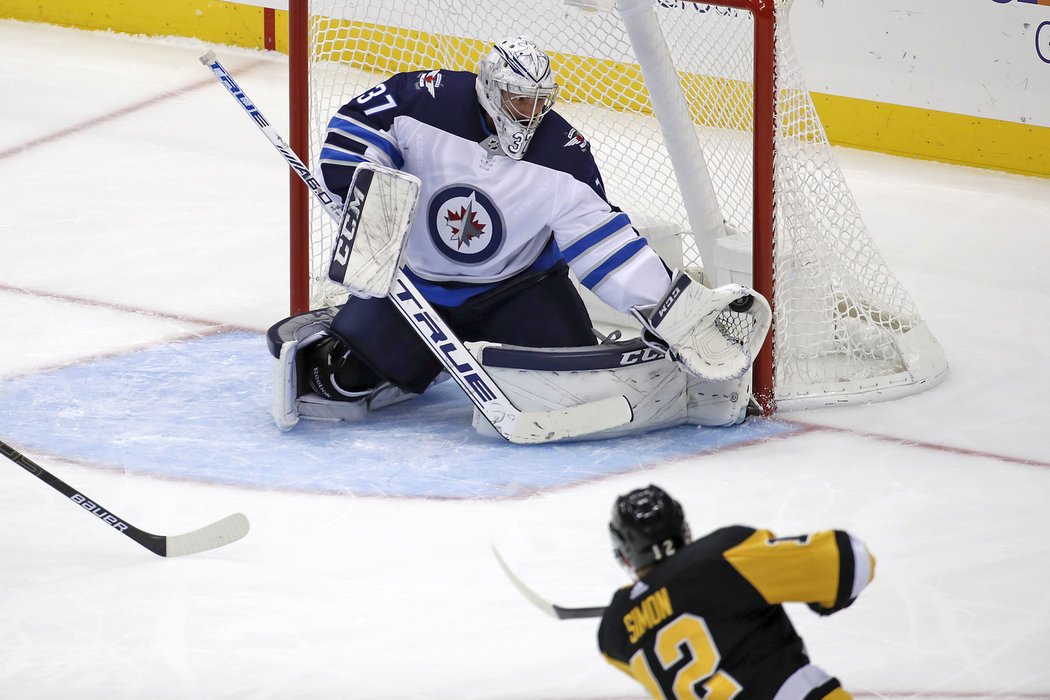 Connor Hellebuyck chytá jednu ze tří střel Dominika Simona v utkání