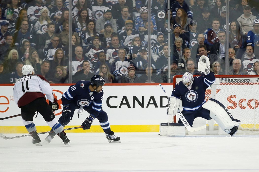 Brankář Winnipegu Connor Hellebuyck efektivně zasahuje lapačkou proti střele Matta Calverta z Minnesoty