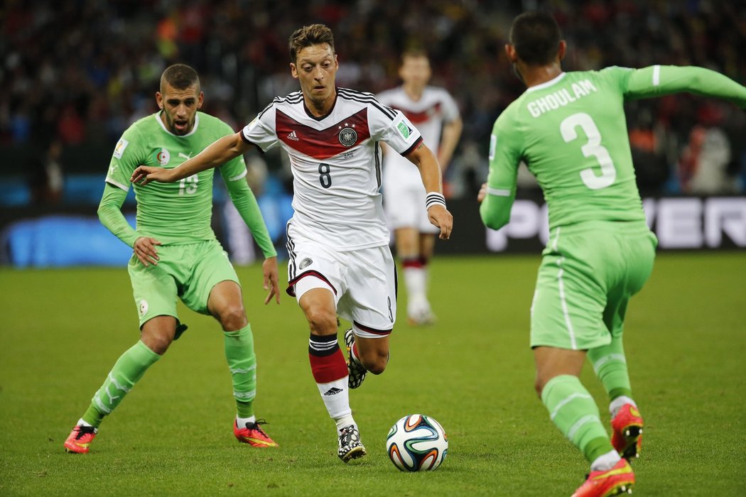 Záložník Německa Mesut Özil v průniku mezi obránci Alžírska