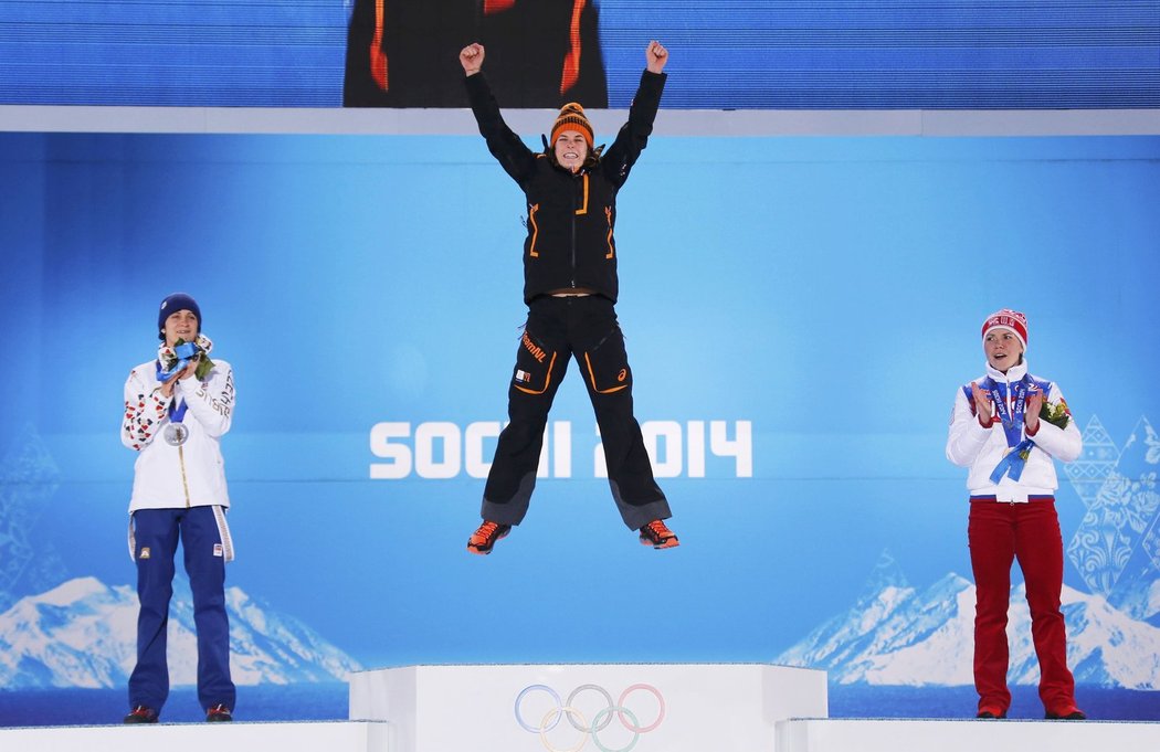 Vítězka Irene Wüstová skáče na stupně vítězů při medailovém ceremoniálu rychlobruslařek, vlevo jí tleská stříbrná Martina Sáblíková, vpravo Ruska Olga Grafová