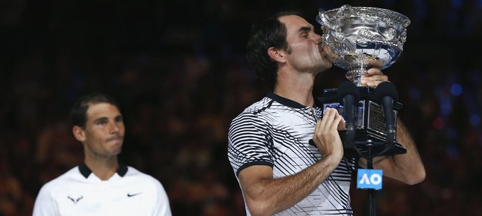 Poražený Rafael Nadal sleduje Rogera Federera s pohárem pro vítěze Australian Open