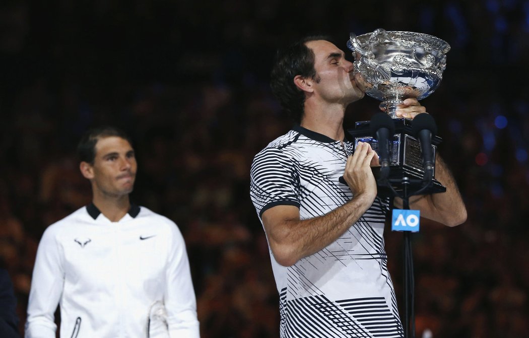 Poražený Rafael Nadal sleduje Rogera Federera s pohárem pro vítěze Australian Open