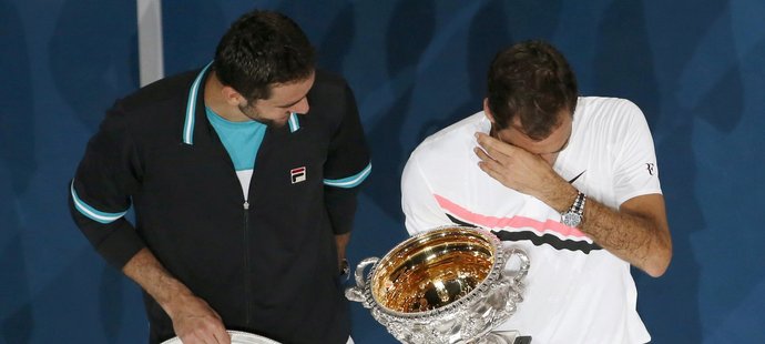 Dojatý Roger Federer utírá slzy s pohárem pro vítěze Australian Open, zatímco k němu mluví poražený finalista Marin Čilič