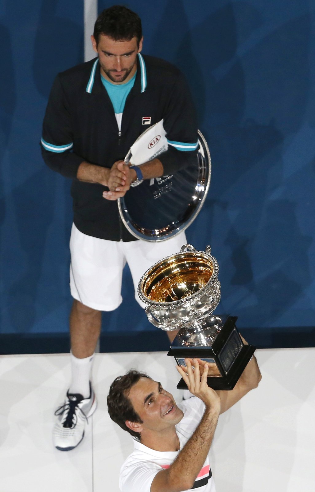 Roger Federer zvedá nad hlavu trofej pro vítěze Australian Open, tleská mu poražený finalista Marina Čilič