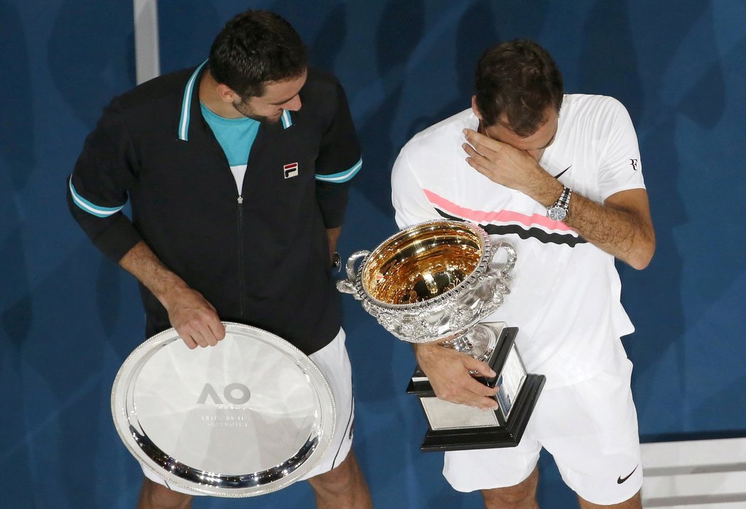 Dojatý Roger Federer utírá slzy s pohárem pro vítěze Australian Open, zatímco k němu mluví poražený finalista Marin Čilič